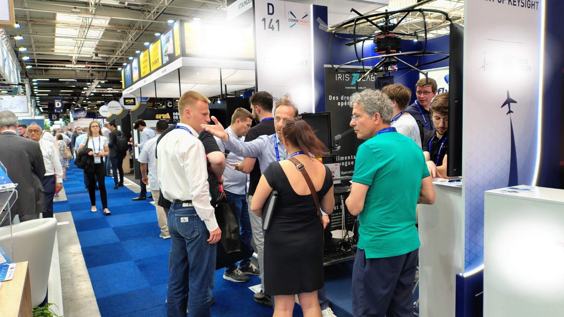 Busy trade show floor with exhibitor staff showing visitors out